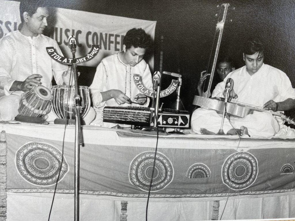 Perhaps from the late-1970’s, we can see musicians wearing white on stage, with Panditji on the slide guitar